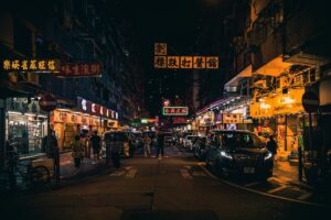 A busy street at night in an Asian city, filled with cars, people, and brightly lit neon signs written in Chinese characters, creating a lively and colorful urban atmosphere.
