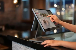 A person uses a touchscreen point-of-sale system at a counter, navigating through a digital menu with food images and options in a modern restaurant setting.