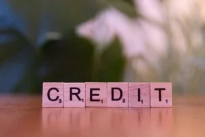 Wooden Scrabble letter tiles arranged to spell the word CREDIT on a wooden surface, with a blurred green background, symbolizing financial growth or a Business Loan.