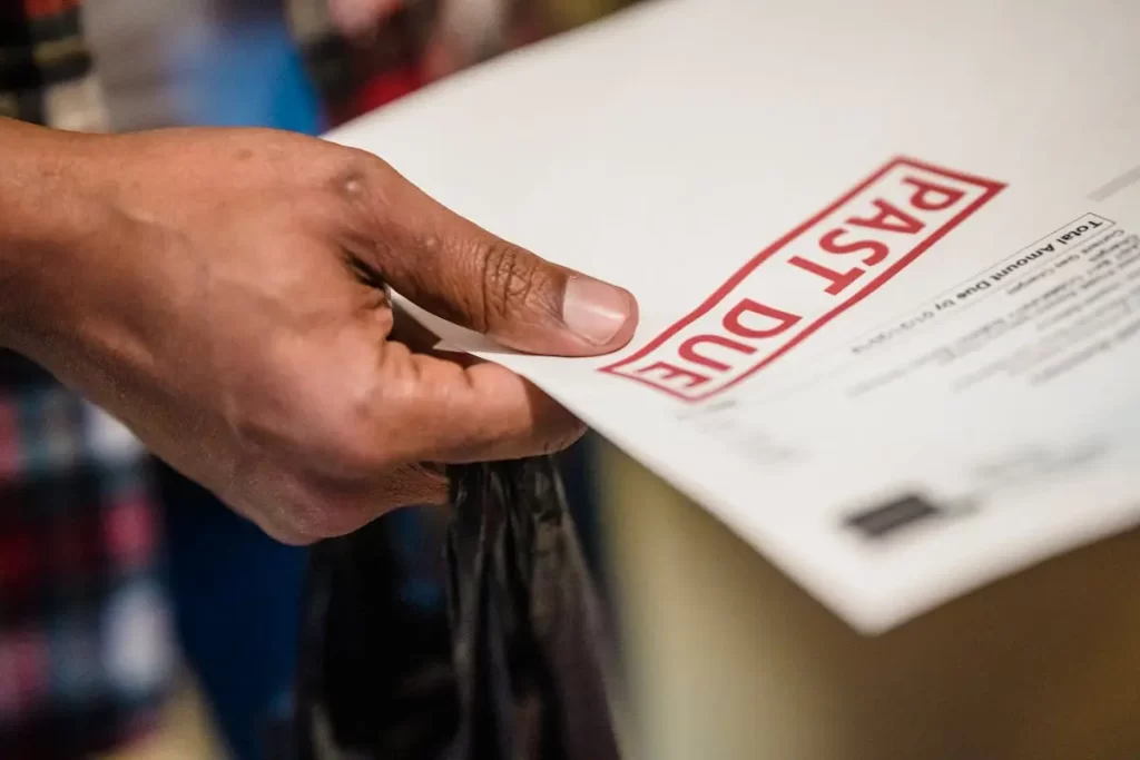 A close-up of a hand holding a white envelope or letter stamped with the words past due in large red letters, indicating an overdue payment notice.