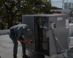 Which Is Better Equipment Lease Or Financing 4 A person in a hat and gray shirt uses a power tool to repair or maintain a large hvac unit on a rooftop during the day.