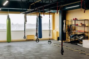 Which Is Better Equipment Lease Or Financing 3 Spacious gym room with punching bags, suspension trainers, agility ladder, and shelves holding various fitness equipment. Large windows let in natural light.
