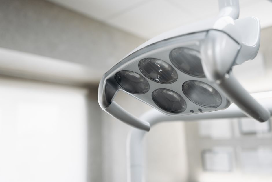 Close-up of a modern dental or medical overhead examination light with multiple round bulbs, in a clean, bright clinical setting.