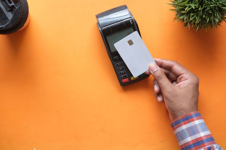 Mca Funding Llc: How It Works &Amp; Costs In 2026 1 A person making a contactless payment with a credit card and card reader on a bright orange surface.