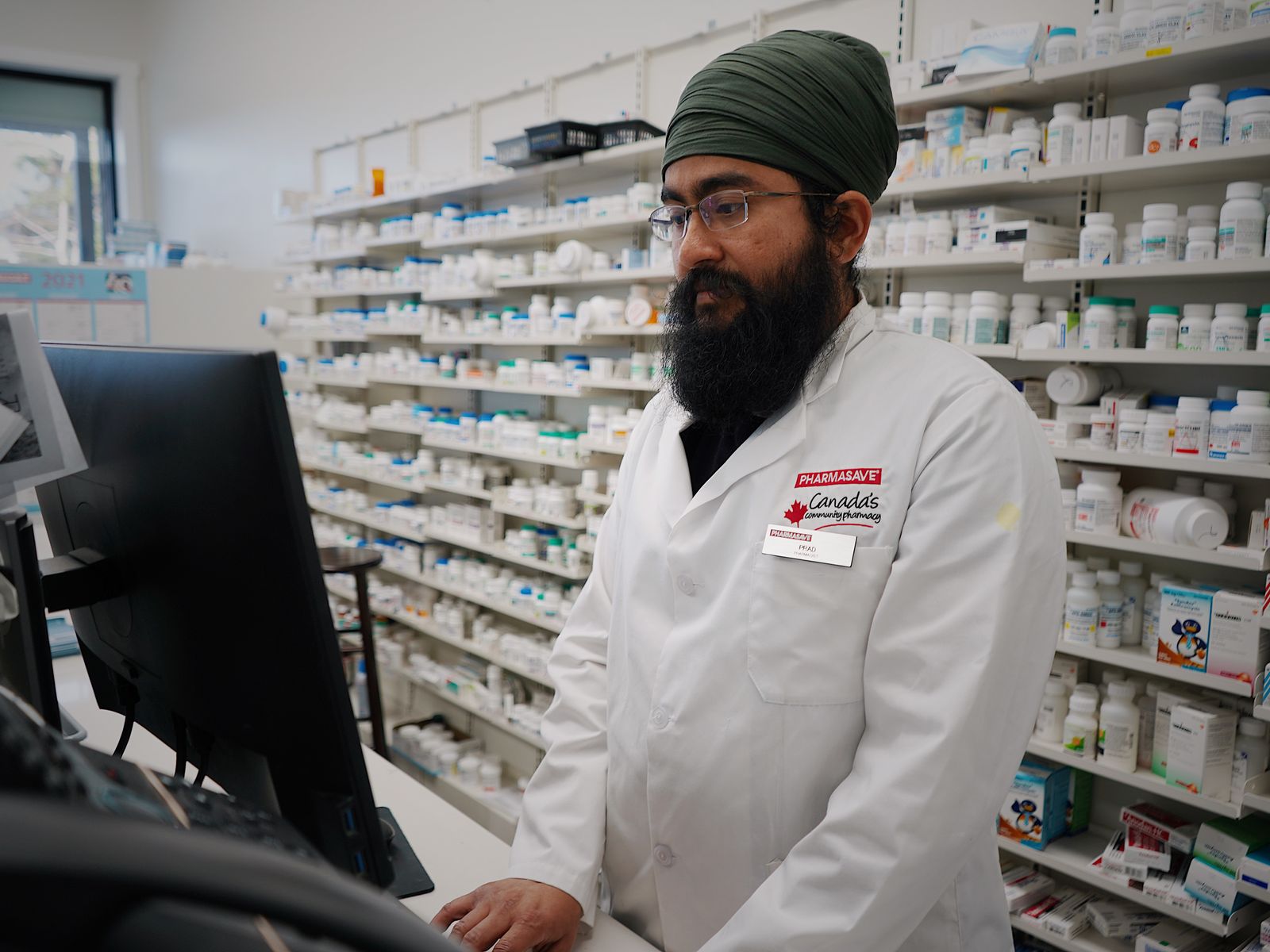 Pharmacist at the counter in front of stocked pharmacy shelves