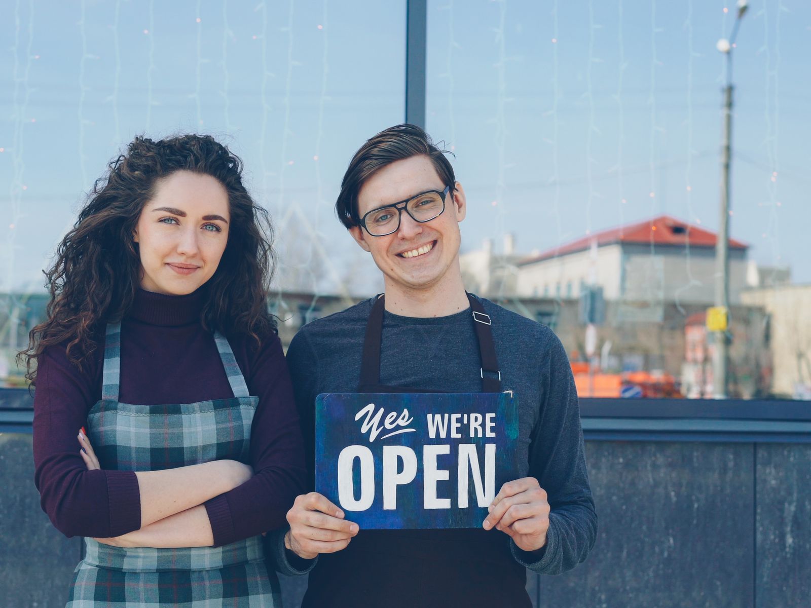 New business owners holding an open sign outside their cafe